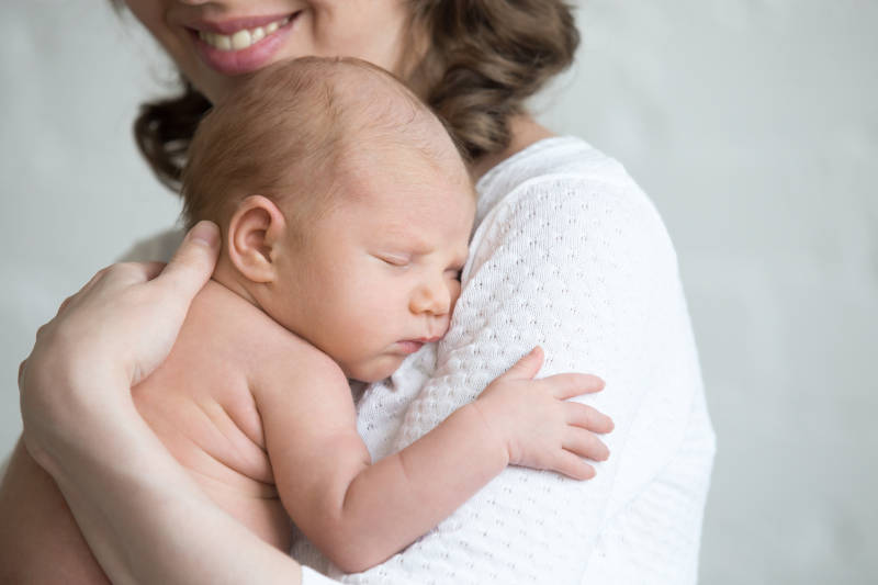 Young happy mother tenderly hugging her newborn baby